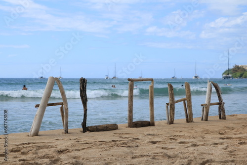 Driftwood Aloha Sign on Beach with sailboats in background