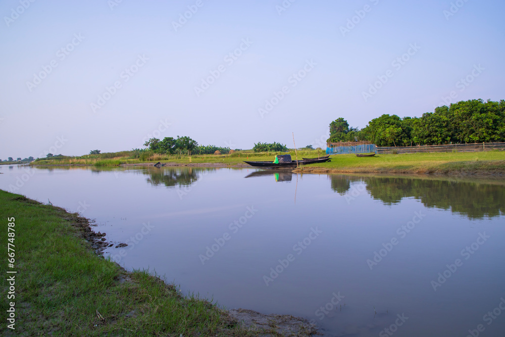 Fototapeta premium Canal with green grass and vegetation reflected in the water near Padma River in Bangladesh