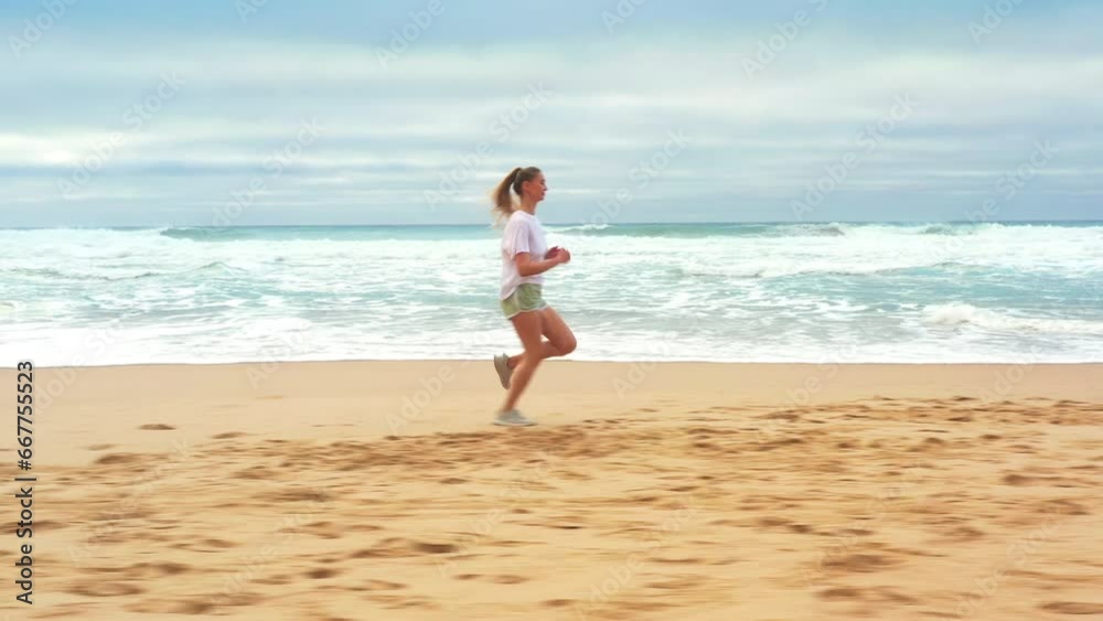 Aerial tracking shot blonde woman jogging along coastline. Young caucasian female exercising outdoors running seashore. Concept of healthy running and outdoors exercise. Summer active Aerial tracking shot blonde woman jogging along coastline. Young caucasian female exercising outdoors running seashore. Concept of healthy running and outdoors exercise. Summer active
