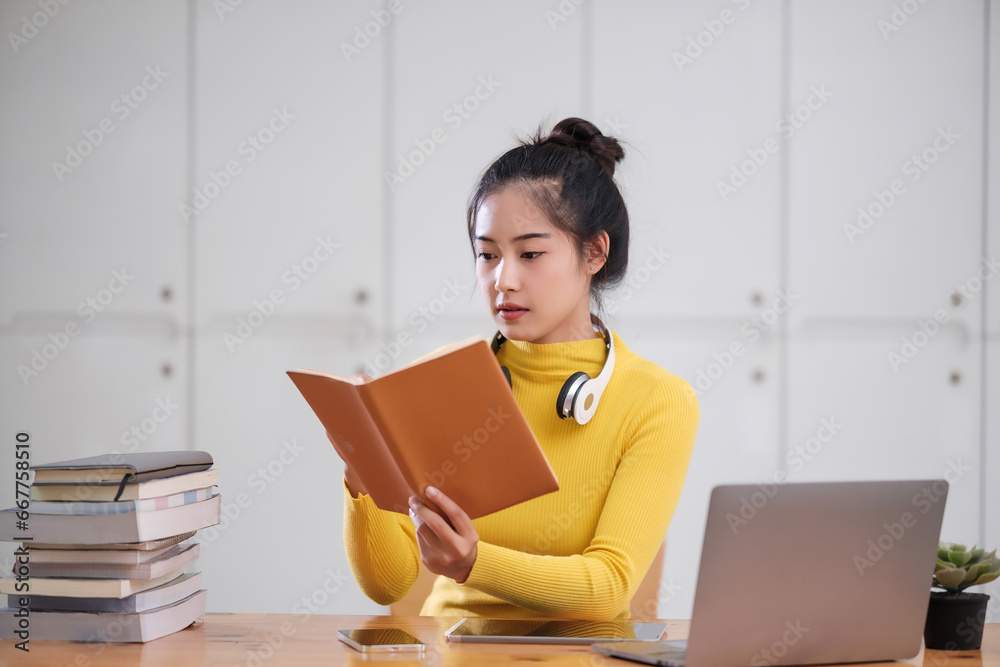 Young adult asian student woman taking notes while using laptop computer at home. Asian female learning online listening virtual video call. Business and education concept. Young adult asian student woman taking notes while using laptop computer at home. Asian female learning online listening virtual video call. Business and education concept.