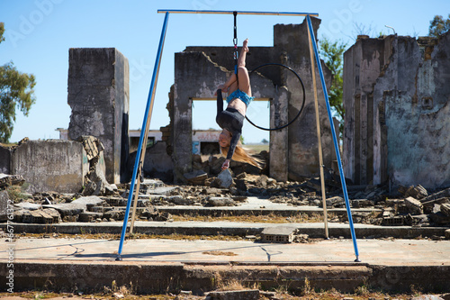 Young and beautiful blonde woman, spectacular exercise on an aerial hoop. She does different artistic and acrobatic poses. The young athlete is among the ruins of a building. Sport concept.
