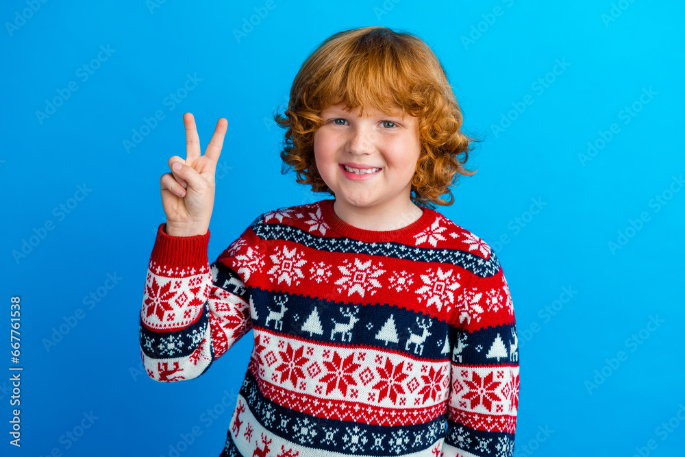 Photo of cool cheerful small boy wear ornament sweater showing v-sign enjoying xmas isolated blue color background Photo of cool cheerful small boy wear ornament sweater showing v-sign enjoying xmas isolated blue color background