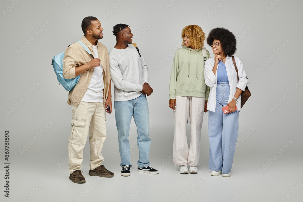 cheerful good looking group of students posing with backpacks on gray background, studying concept