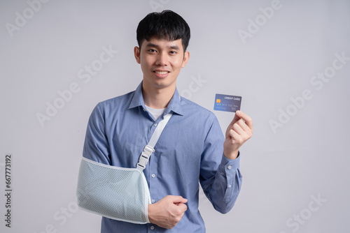 Injured asian man patient accident broken hand soft splint arm showing mock up credit card standing on white background. Smile young girl hold empty card over isolated.Insurance accident health care