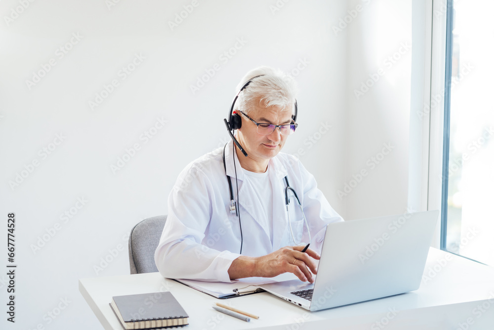 Middle aged male doctor using headset and laptop for online video call consulting of patient. Telemedicine concept for domestic health treatment. Online remote medical appointment. Medical technology. Middle aged male doctor using headset and laptop for online video call consulting of patient. Telemedicine concept for domestic health treatment. Online remote medical appointment. Medical technology.