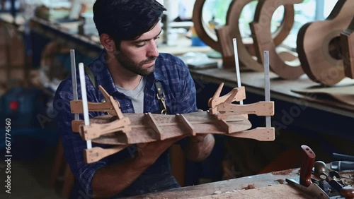 Luthier creating a guitar and using tools in a traditional, clamps on the body of a guitar under construction improving glue adhesion photo