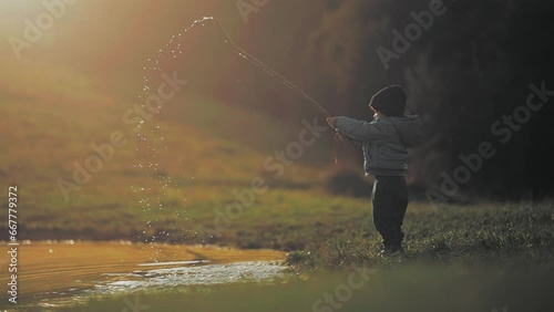 Child playing with water in a lake. He makes the drops splash with a stick
