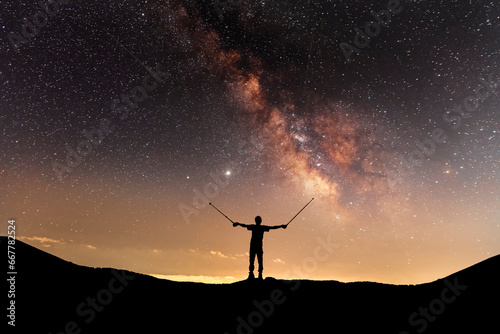 Silhouette of a hiker standing on the hill, on the milky way galaxy background.