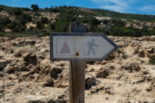 Metal old rusty sign with hiking symbol on wooden pole, Gavdos island, Crete Greece, blur background