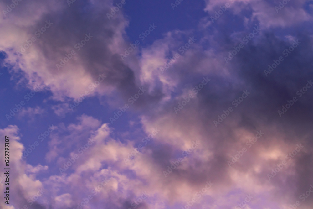 Gray and pink shaded cumulus clouds, floating under a blue sky during twilight.