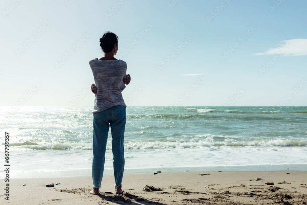 A beautiful brunette girl stands barefoot on the sandy seashore, enjoying the nature A beautiful brunette girl stands barefoot on the sandy seashore, enjoying the nature