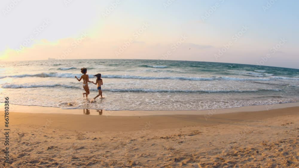 Happy beautiful young mother and her son are running along the sand on the sea beach, smiling and having fun together. Family holiday at sea. Happy beautiful young mother and her son are running along the sand on the sea beach, smiling and having fun together. Family holiday at sea.