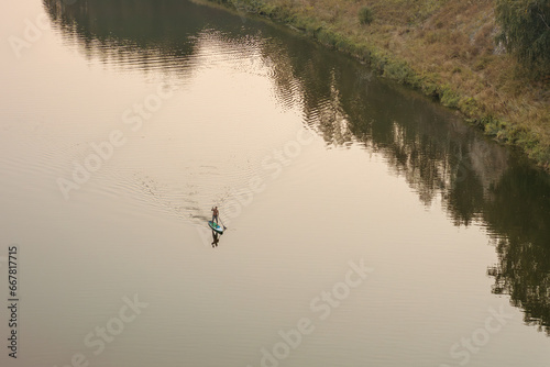 a man is floating on a sapboard on the river, a man is rowing with an oar on the water surface photo