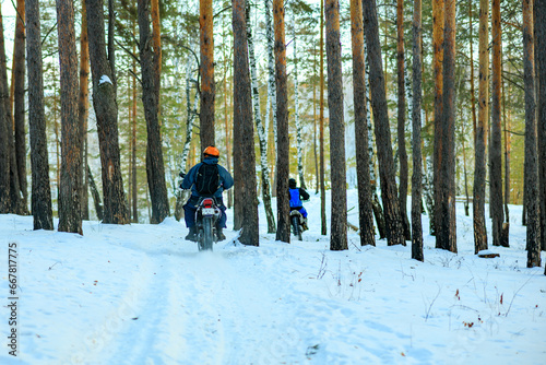 two motorcyclists in the winter forest among the trees.