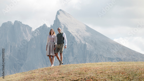 Mann und Frau stehen Hand in Hand in Tracht inmitten der Berge der Dolomiten