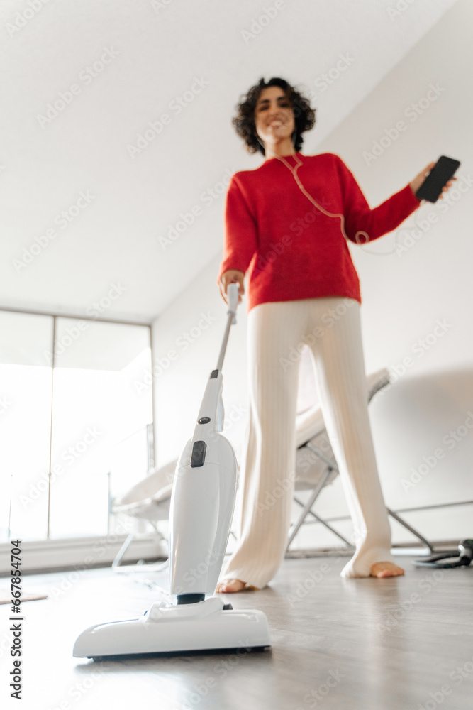 Low angle view of the joyful woman cleaning home with vacuum cleaner Low angle view of the joyful woman cleaning home with vacuum cleaner