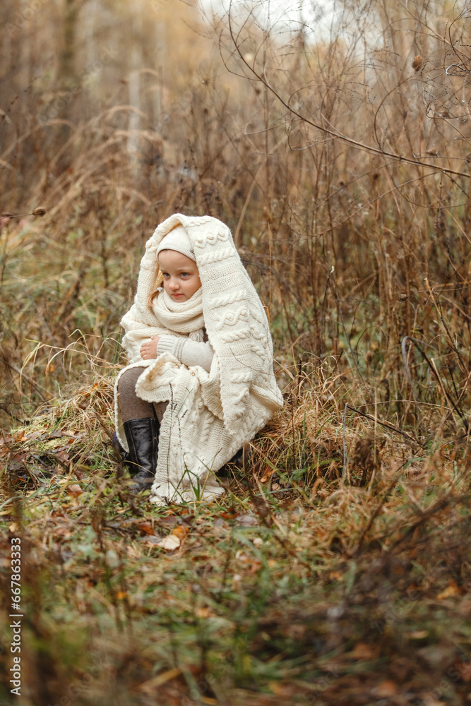 Portrait of a smiling young girl sitting in a park wrapped in a white blanket. Portrait of a smiling young girl sitting in a park wrapped in a white blanket.