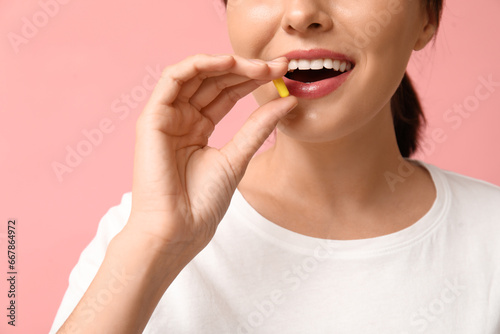 Woman taking pill on pink background  closeup