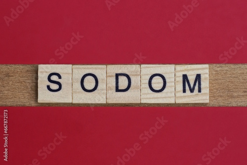 text the word sodom from gray wooden small letters with black font on an red table