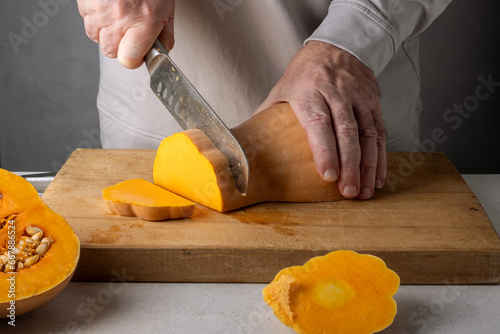 Caucasian unrecognizable middle-aged man cutting pumpkin on a wooden cutting board. Selective focus.