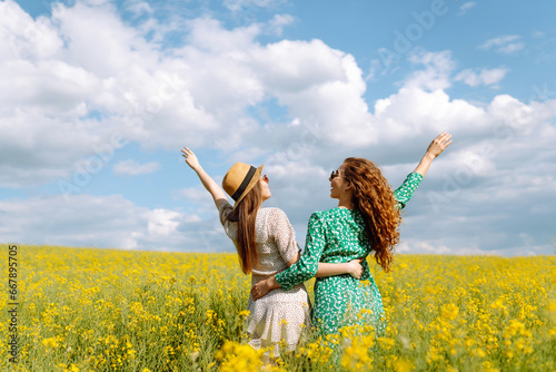 Two cheerful girlfriends have a great summer time walking through a blooming rapeseed field. The concept of walking, active lifestyle, holidays.