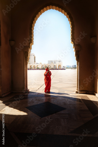 Full length silhouette of a Muslim Arabian woman in hijab and traditional clothes standing under marble arch of mosque
