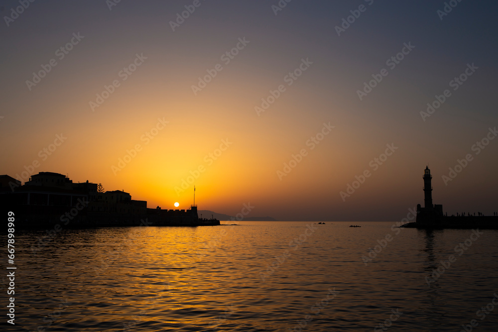 Sunset landscape in Chania's harbour with lighthouse silhouette on quiet Mediterranean waters
