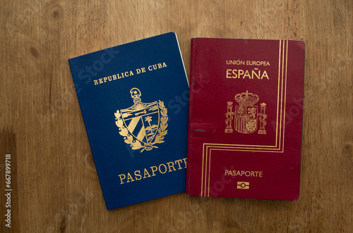 spanish dark red passport over a blue Cuban passport on a woody background photo