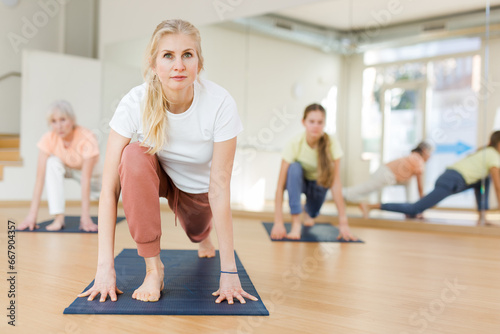 Woman exercising yoga pose during group training in studio.