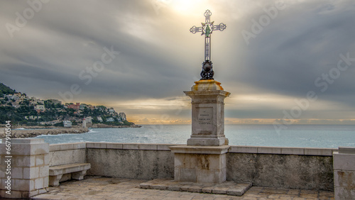 Une croix religieuse en bord de mer dans les lueurs du soleil  émergeant des nuages photo