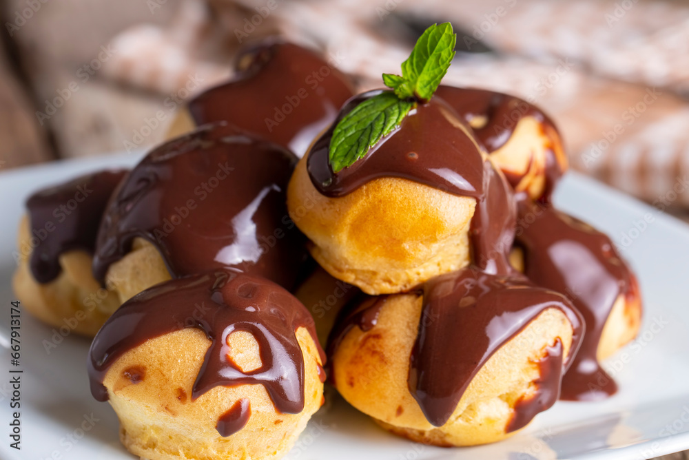 Delicious profiteroles with chocolate and white plate. Selective focus image on light background.