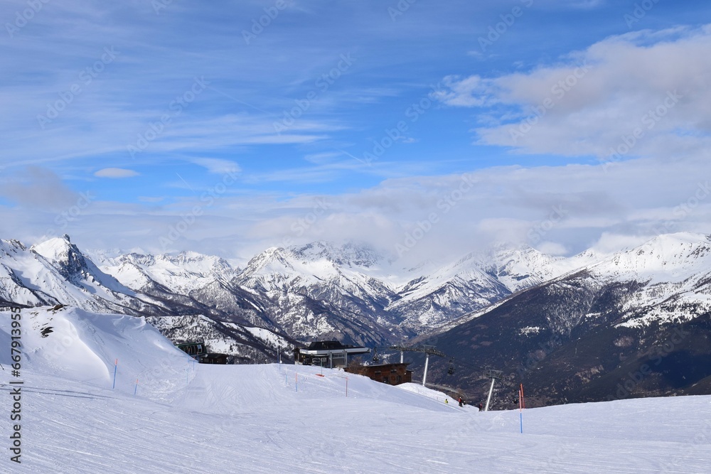 Stunning view of Italian mountain range and valley from ski slope in Sauze D'Oulx ski resort, Turin, Italy. Beautiful Italian alpine peaks of snow capped mountains in the Piedmont region.