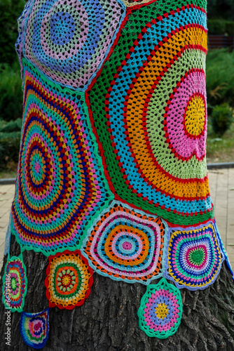 Colorful crochet knit on tree trunk in Kyiv, Ukraine. Street art goes by different names, graffiti knitting, yarn bombing. Abstract background of knitted rugs with a multicolored circles pattern