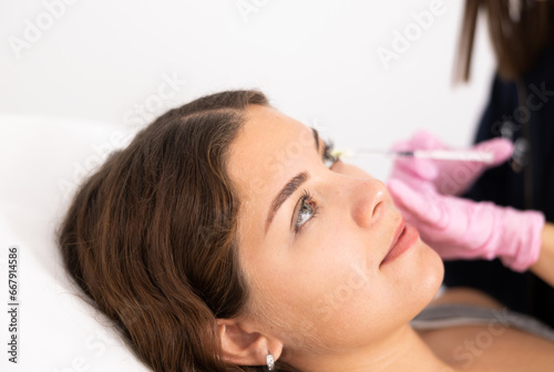 Close-up view of young woman's face undergoing mesotherapy procedure by injection in aesthetic cabinet