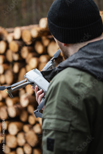 A man holding a drone and preparing him for flight against the background of rubbed wood in the forest (selective focus)