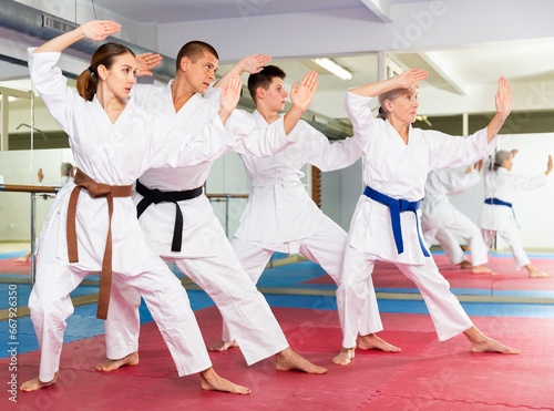 Concentrated people of different ages in kimonos practicing punches in gym during group martial arts workout. Shadow fight, combat sports training concept ..