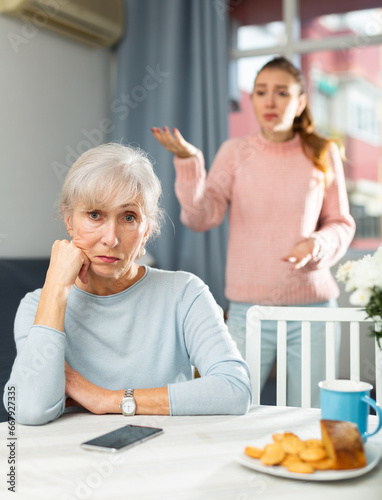 Sad elderly woman having quarrel with her daughter. She's sitting at table and listening her daughter swearing. © JackF