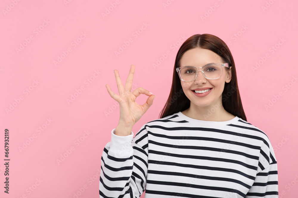 Smiling woman in stylish eyeglasses showing ok gesture on pink background. Space for text Smiling woman in stylish eyeglasses showing ok gesture on pink background. Space for text