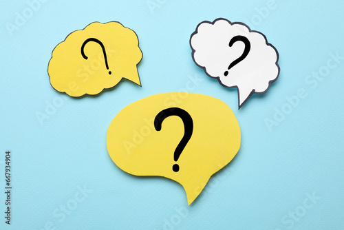 Paper speech bubbles with question marks on light blue background, flat lay