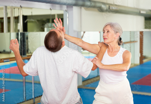 Elderly woman is training with man on the self-defense course in gym