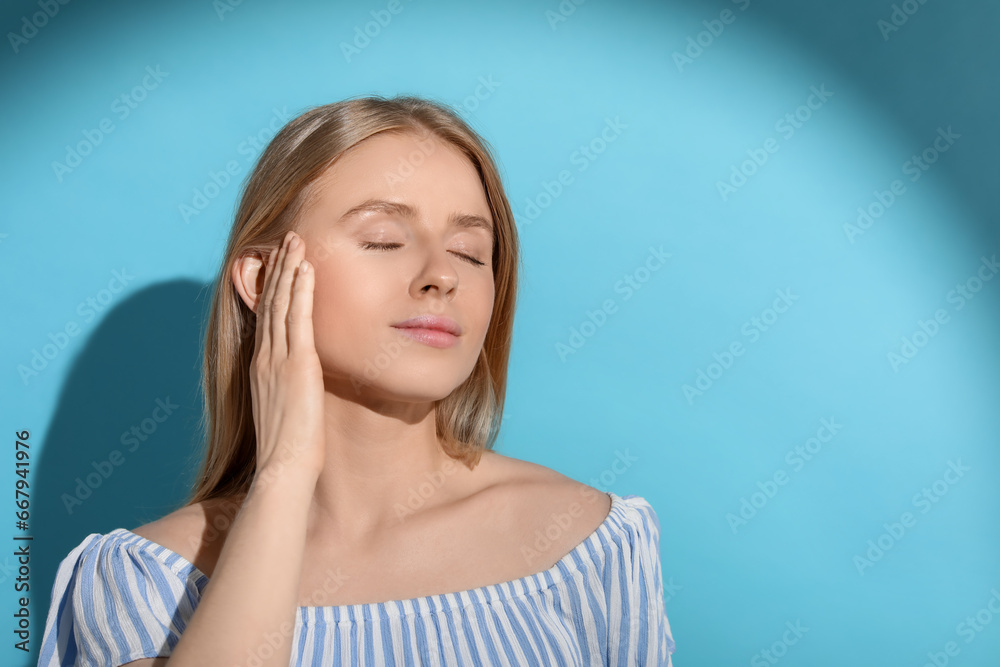 Beautiful young woman in sunlight on light blue background, space for text Beautiful young woman in sunlight on light blue background, space for text