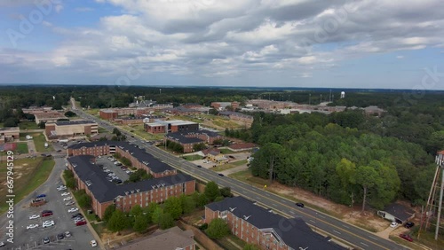 descending aerial footage of Grambling State University with red brick buildings surrounded by green trees and grass, cars driving on the street, blue sky and powerful clouds in Grambling Louisiana photo