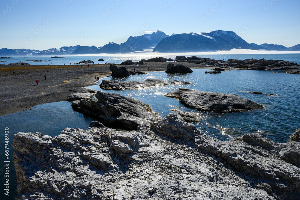 Cold adventure with people exploring the beach of Gnalodden on a sunny blue sky day, arctic expedition tourism around Svalbard
