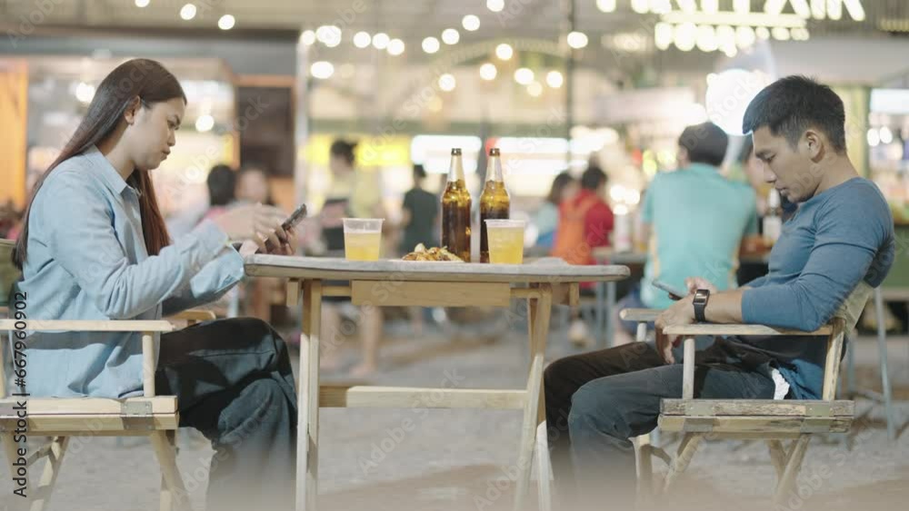 Asian tourist couple using smartphone and drinking beer at night market in Thailand Asian tourist couple using smartphone and drinking beer at night market in Thailand
