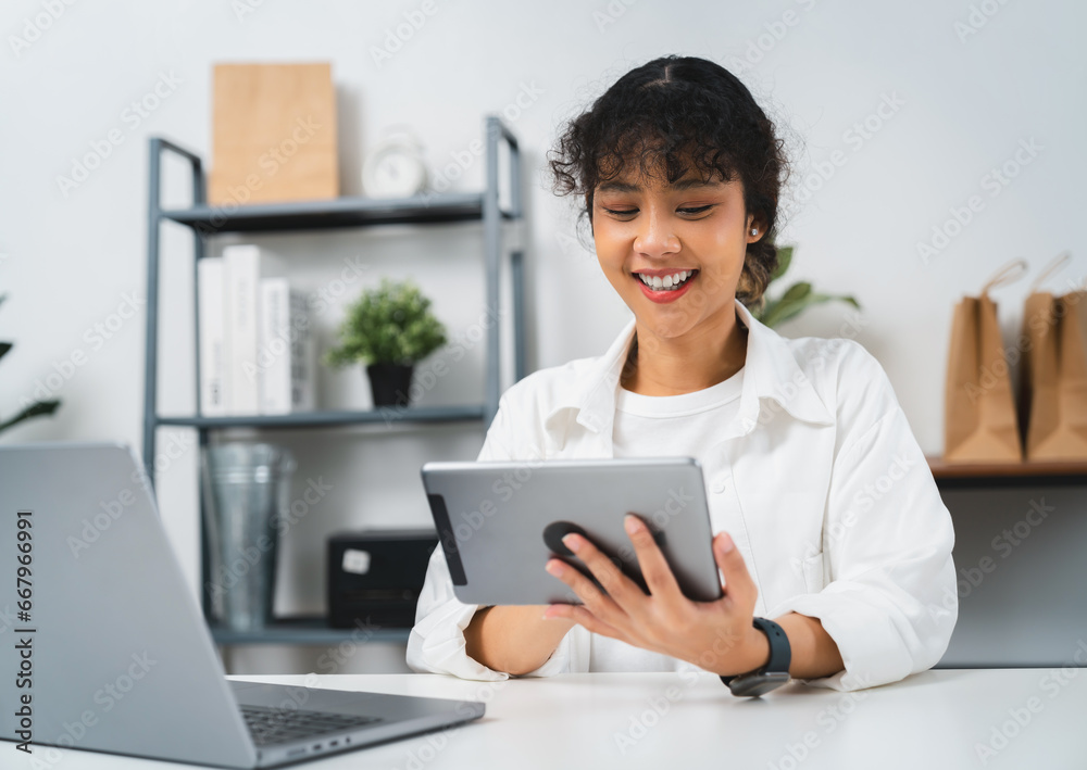 Happy young Asian woman using digital tablet and checking email inbox, social media messages on the table in modern home. Happy young Asian woman using digital tablet and checking email inbox, social media messages on the table in modern home.