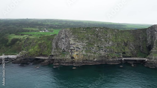 Aerial panning shot of majestic cliffs on the blue sea from the Gobbins Cliffs during an adventurous trip through Northern Ireland on a calm morning photo