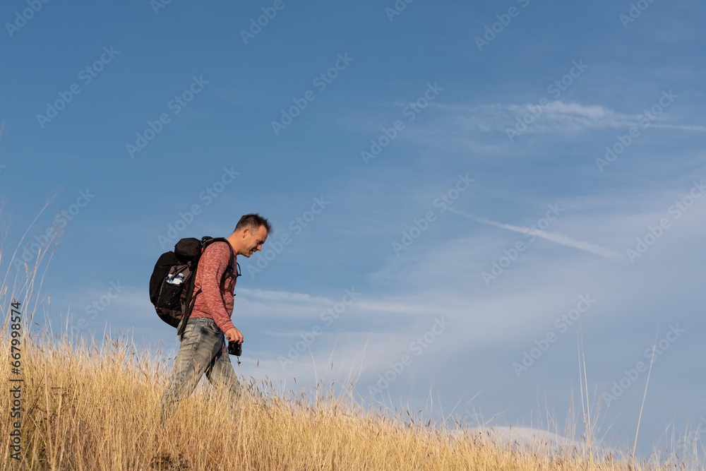 Young man hiking through autumn fields and hills against blue sky during warm day. Weekend, leisure, sport Young man hiking through autumn fields and hills against blue sky during warm day. Weekend, leisure, sport