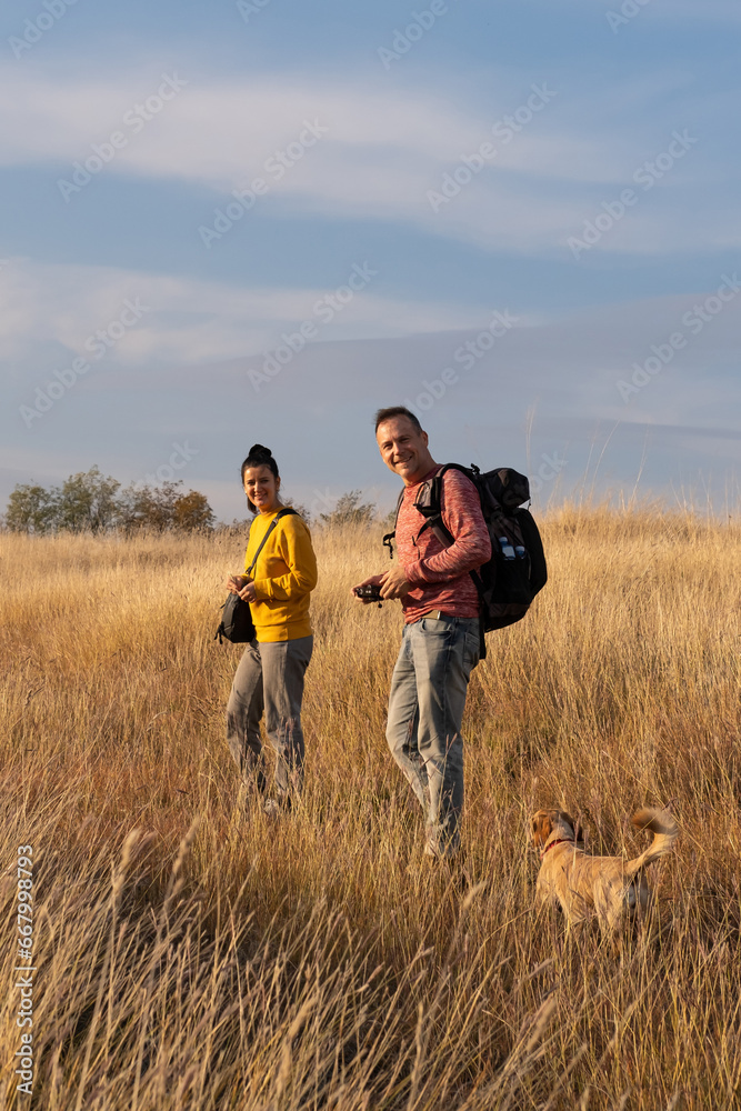 Young couple hiking through autumn fields and hills during warm day with their dog. Weekend, leisure, sport Young couple hiking through autumn fields and hills during warm day with their dog. Weekend, leisure, sport