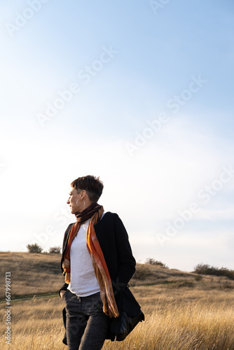 Young woman hiking through autumn fields and hills against blue sky during warm day. Weekend, leisure, sport