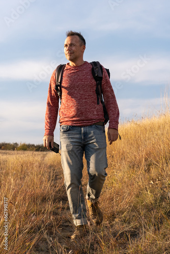 Young man hiking through autumn fields and hills against blue sky during warm day. Weekend, leisure, sport